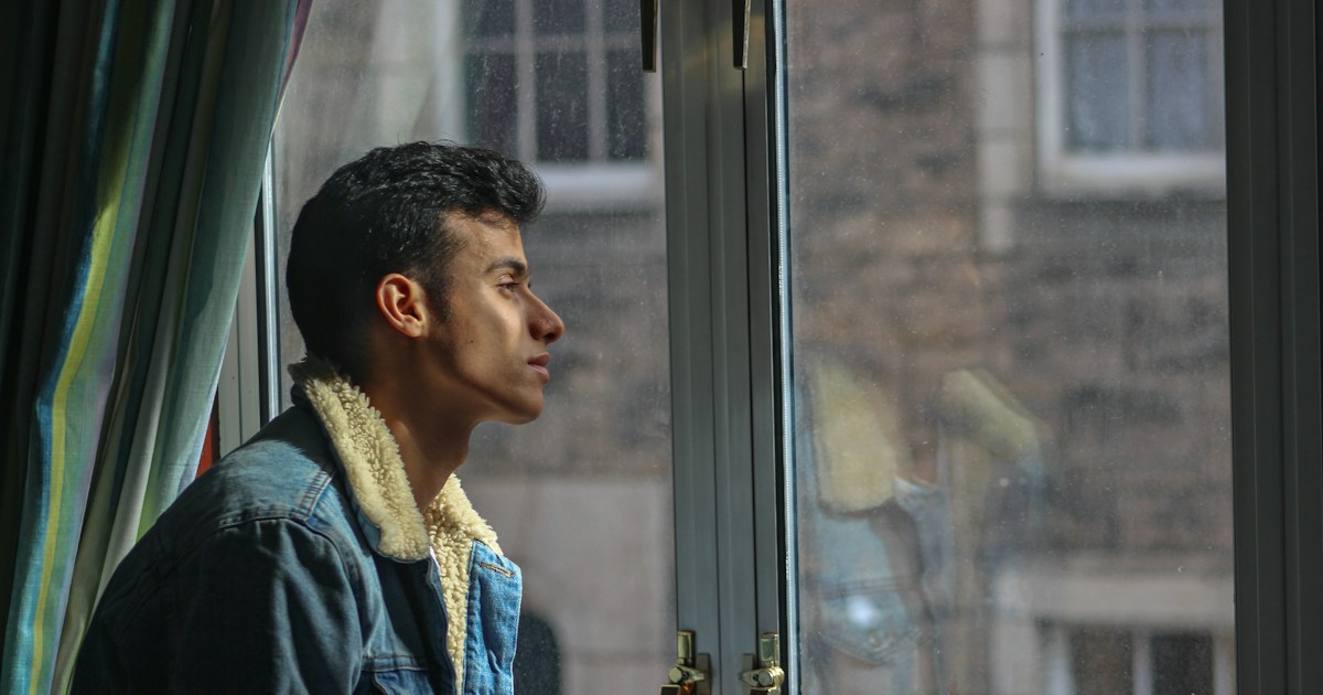 Hombre en penumbra mira hacia la luz desde una ventana, imagen del deseo de ver y comprender