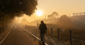 Una persona camina por una carretera entre la niebla iluminada por el amanecer.